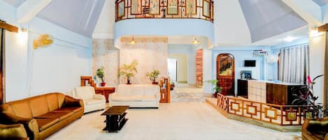 A spacious living area with a high ceiling, a balcony with a railing, and a reception desk.