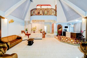 A spacious living area with a high ceiling, a balcony with a railing, and a reception desk. - Fabexpress The Dove (Guwahati)