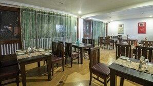 A dining area with multiple tables and chairs, a window with curtains, and a wall with framed pictures. - Xomotel Bungalows Krishanya (Nainital)