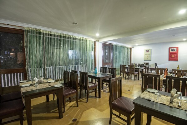 A dining area with multiple tables and chairs, a window with curtains, and a wall with framed pictures.
