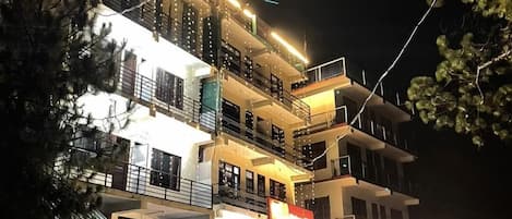 A multi-story hotel with balconies, a visible restaurant, and a parking lot with cars.
