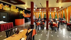 A restaurant with multiple tables and chairs, a decorative wall, and large windows with curtains. - The Udai Bagh (Māvli)
