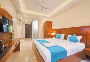A hotel room with a bed, bedside tables, a TV, a ceiling fan, and a wardrobe. - Hotel Green One Earth (Yamkeshwar)