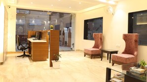 Un espacio de oficina moderno con un mostrador de recepción, dos sillas con diseños, una mesita y una mesa de centro de vidrio.
