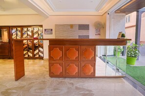 A reception desk with a wooden panel design, a tiled wall, and a small potted plant. - Hotel Green One Earth (Yamkeshwar)