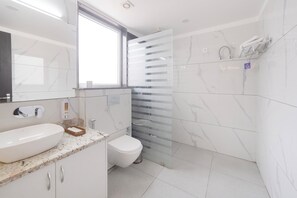 A modern bathroom with a white sink, toilet, and shower area. - Hotel Green One Earth (Yamkeshwar)