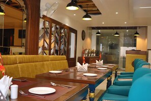 A dining area with wooden tables, blue upholstered chairs, and a decorative partition. - Hotel Green One Earth (Yamkeshwar)