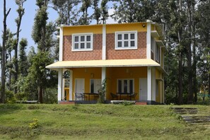 A two-story building with a yellow facade and white trim, surrounded by trees. - River Valley Resort Masinagudi (Ootacamund)