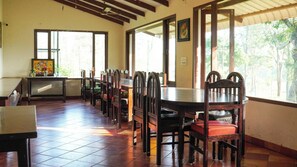 A dining area with wooden tables and chairs, large windows, and a tiled floor. - River Valley Resort Masinagudi (Ootacamund)