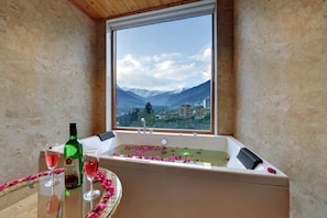 Un bagno con una vasca, una finestra vista montagna e petali di rosa sul pavimento.