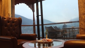 Quarto com vista para montanhas, uma poltrona de couro, uma mesa redonda com um prato de comida e uma pequena planta.