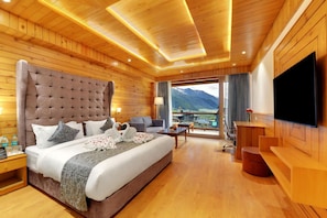 A hotel room with a large bed, a TV, a balcony with a mountain view, and wooden paneling. - Tiaraa Hotels & Resorts - Manali (Manali)