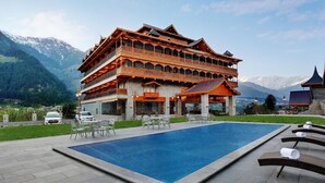 Um edifício com vários andares, piscina, área de estar ao ar livre e montanhas ao fundo.
