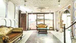 Una habitación amplia con piso de mármol, un sofá antiguo, un ventilador de techo y vistas a través de amplios ventanales.