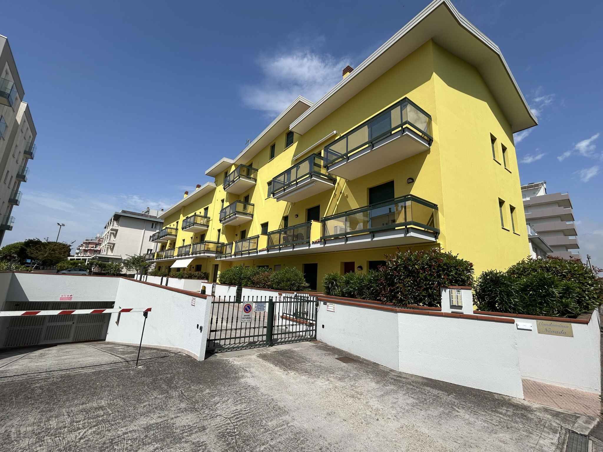 A multi-story yellow building with balconies, a gated entrance, and a clear sky.
