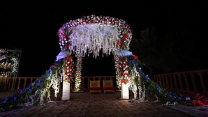 Um arco floral ornamentado com decorações penduradas e duas estátuas.