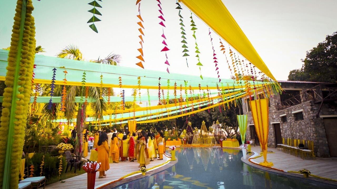 A poolside area with a gathering of people, a stone building, and a yellow canopy.