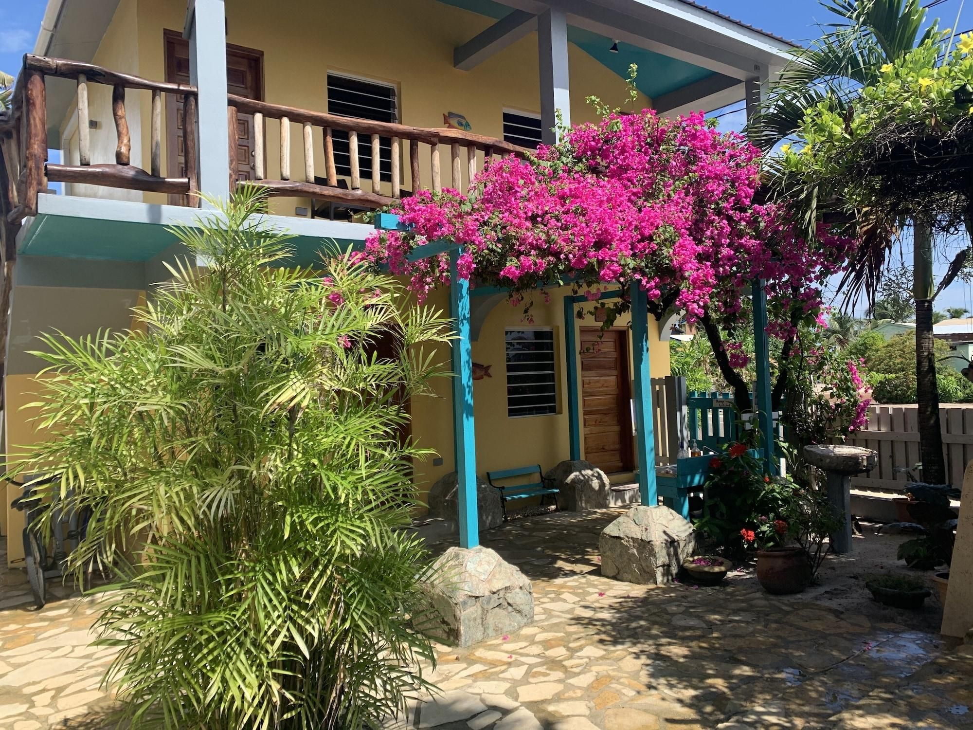 A two-story building with a balcony, a stone-paved courtyard, and a vibrant pink flowering plant.