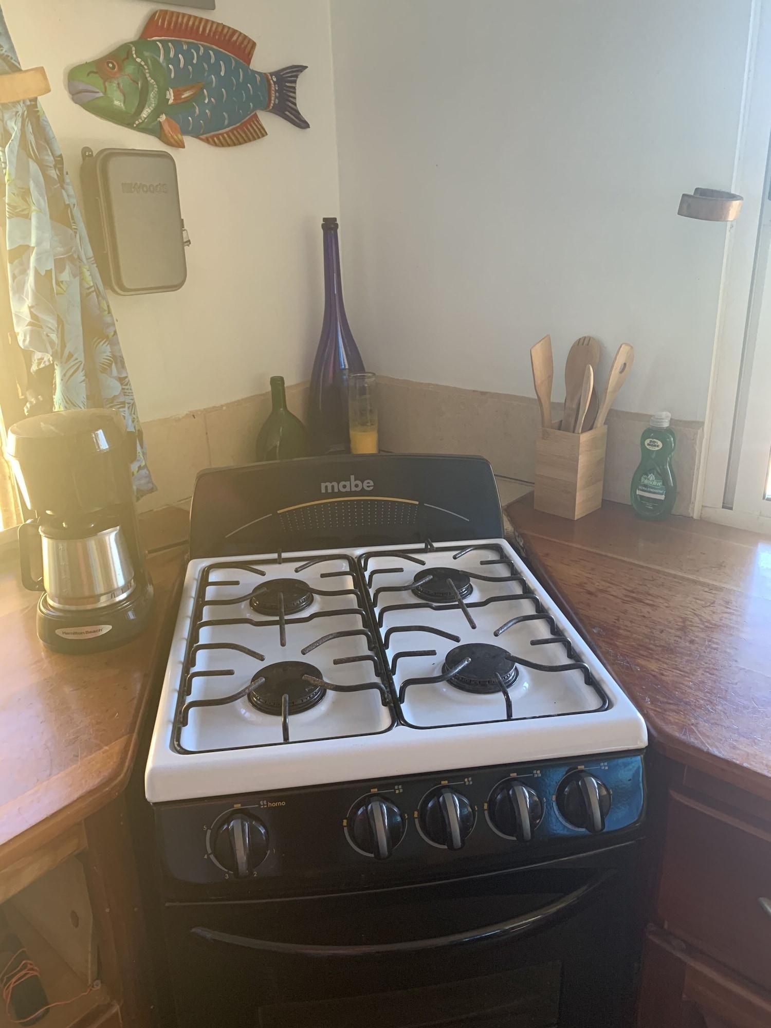 A kitchen with a stove, a coffee maker, a bottle, and wooden utensils.