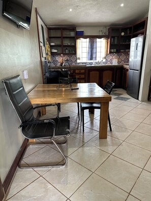 Una cocina con una mesa y sillas de madera, un refrigerador y una ventana con cortinas.