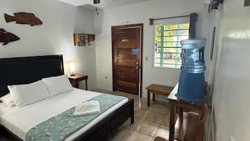 A bedroom with a bed, a ceiling fan, a wooden door, a window, and a water dispenser.