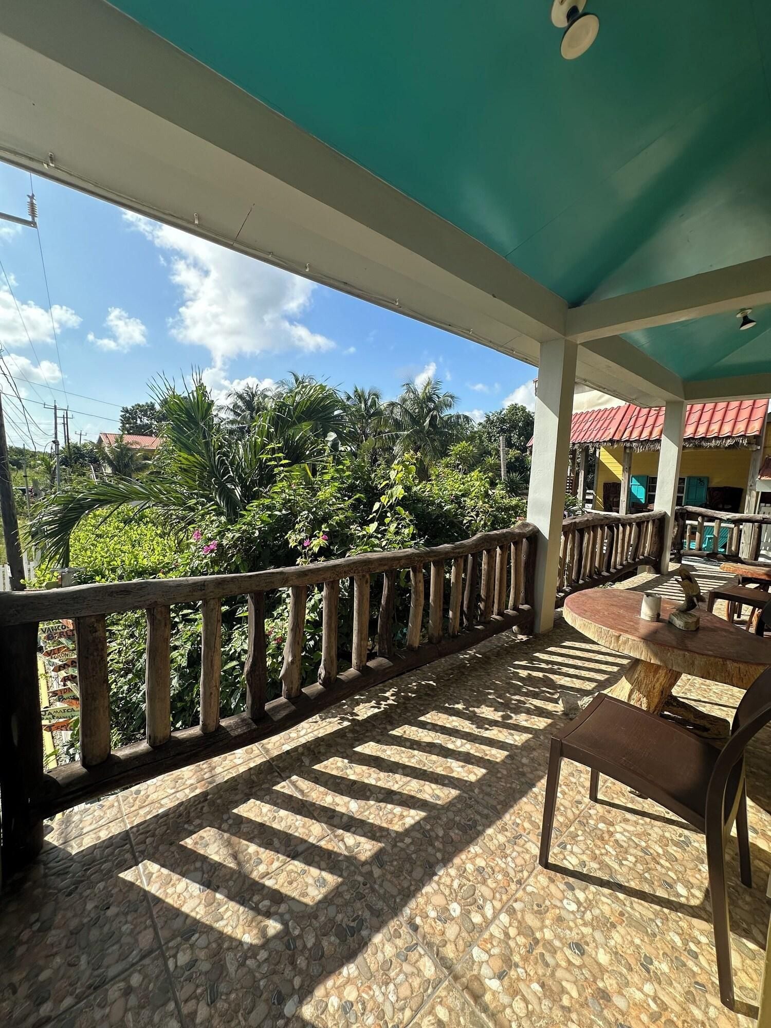 A covered outdoor area with a stone-tiled floor, a wooden railing, and a view of greenery and buildings in the distance.