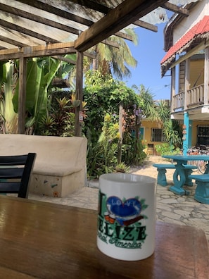 A table with a mug, a bench, and a covered area with plants and a building in the background. - All Seasons Guest House (Hopkins)