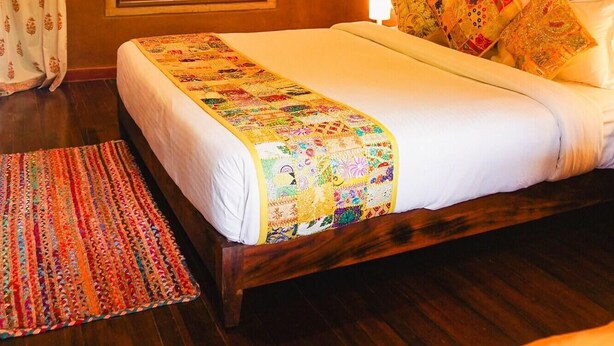 Een slaapkamer met een houten bed, een kleurrijke quilt, gestreepte kussens, een raam en een gordijn.
