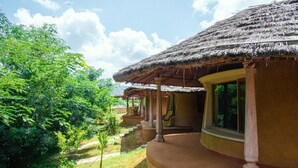 Een traditionele structuur met rieten dak en een overdekte veranda, omringd door weelderige begroeiing.