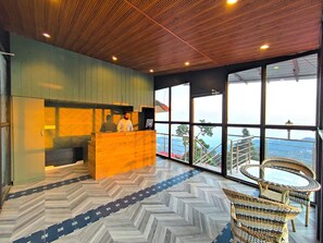 A reception desk with a view of the mountains through large windows. - Sangam By Stotrak - Mussoorie (Dehradun)