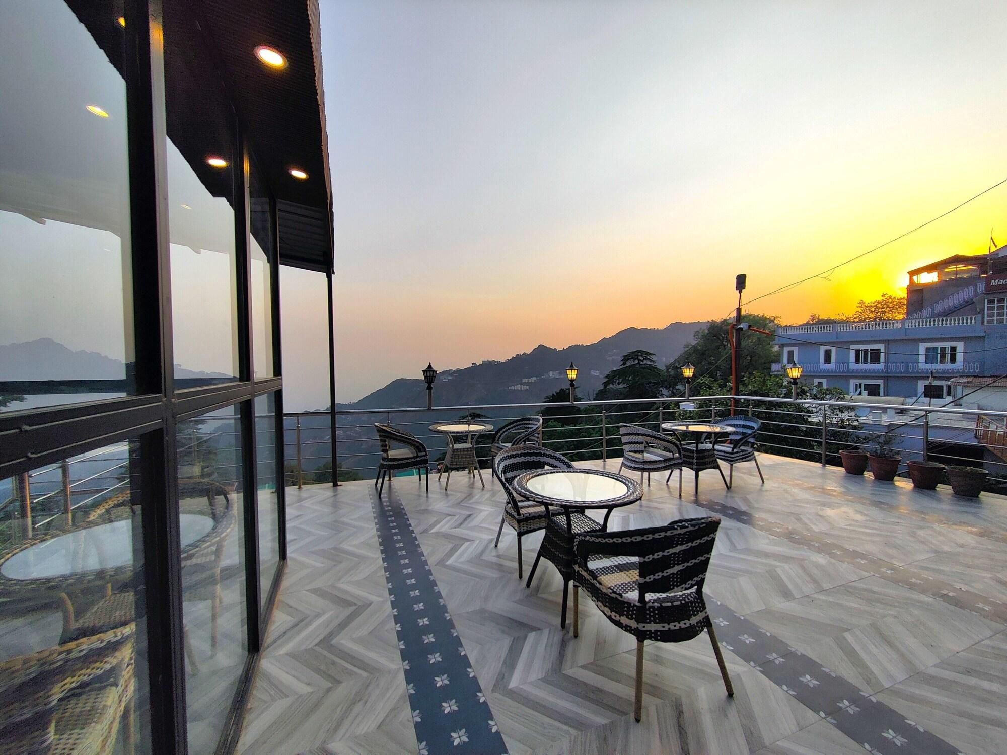 A terrace with outdoor seating, a view of the mountains, and a building in the background.