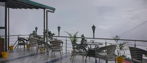 Una terraza con sillas y mesas de mimbre, plantas en macetas y vistas al cielo.