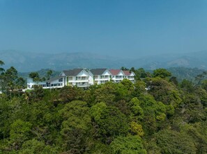 A multi-story hotel with a modern architectural style, surrounded by lush greenery and mountains in the background. - Sprise Munnar-resort & Spa (Devikolam)