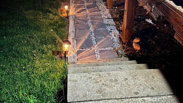 A stone pathway leading to a wooden deck with railings, surrounded by grass and illuminated by wall-mounted lights. - CLOSE TO STADIUM! 2-bdroom lower level open-concept home (Kansas City)