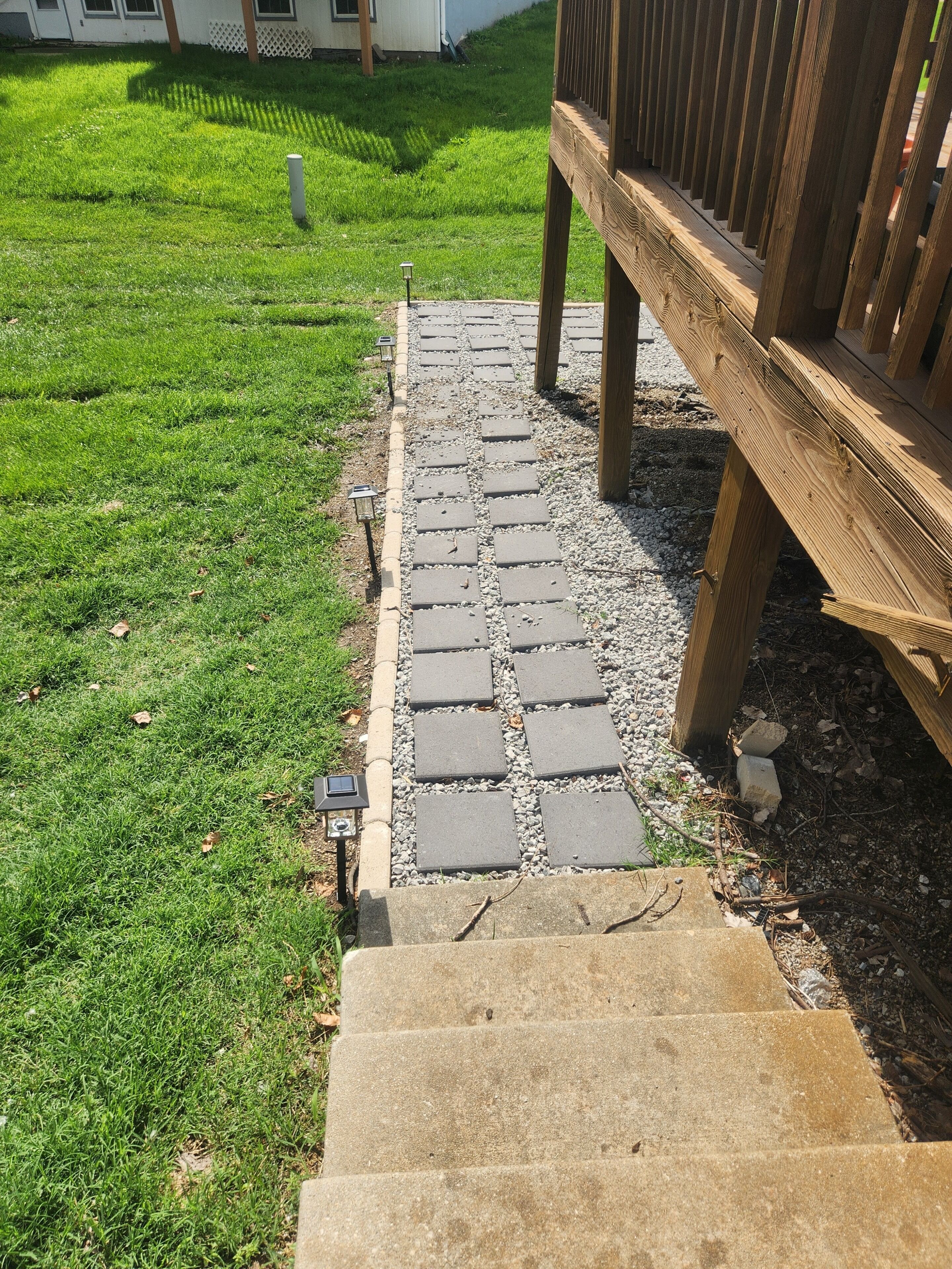 A stone pathway leading to a wooden deck, surrounded by a well-maintained lawn.. CLOSE TO STADIUM! 2-bdroom lower level open-concept home