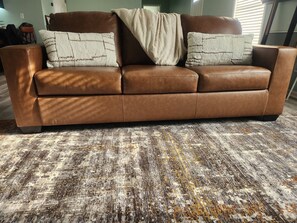 A brown leather sofa with two white pillows and a beige throw blanket, placed on a patterned carpet. - CLOSE TO STADIUM! 2-bdroom lower level open-concept home (Kansas City)