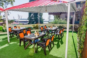 An outdoor patio with tables and chairs, a covered area, and a view of buildings in the background. - The Kenilworth Mussoorie (Dehradun)