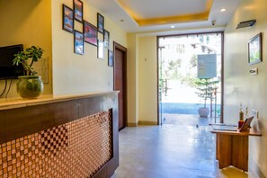 A reception area with a tiled counter, framed pictures on the wall, and a potted plant. - The Kenilworth Mussoorie (Dehradun)