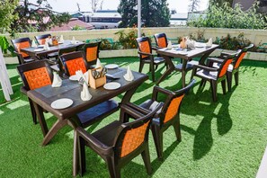 Outdoor dining tables with chairs, arranged on artificial grass, surrounded by greenery. - The Kenilworth Mussoorie (Dehradun)