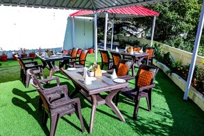 An outdoor patio with tables and chairs, surrounded by potted plants and a green lawn. - The Kenilworth Mussoorie (Dehradun)