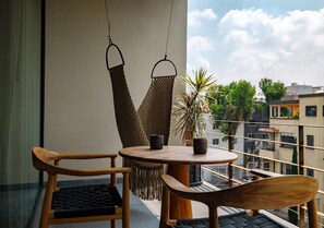 A balcony with a round table, two wooden chairs, a hanging hammock, and a potted plant. - Colima 71 Art Community Hotel (Mexico City)