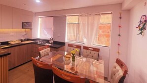A modern kitchen with a central island, dining table with chairs, and a view of the outside through large windows. - APARTMENTS ALEXIA HOUSE ENJOY A COMFORTABLE AND COZY STAY IN CUSCO (Cusco)