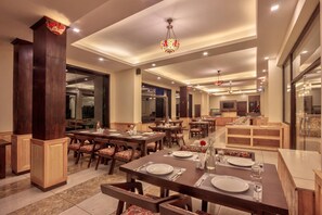 A spacious dining area with multiple tables and chairs, a central chandelier, and a large mirror on the wall. - Katoch Grand By Vivaan (Manali)