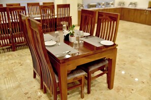 A dining table set with chairs, a plant, and tableware. - Hotel Aarna (Jaipur)