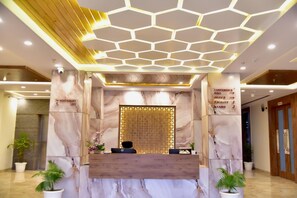 A hotel reception area with a marble reception desk, a digital screen, a conference hall sign, and a staircase sign. - Hotel Aarna (Jaipur)
