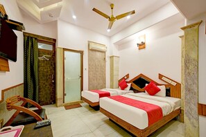 A hotel room with two beds, a ceiling fan, a TV, and a desk with a remote control. - Hotel Natraz New Delhi (New Delhi)