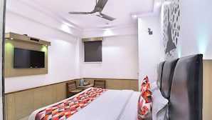 Habitación de hotel con cama, televisor de pantalla plana montado en la pared, ventilador de techo y un adorno mural.