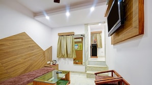 Una sala moderna con un sofá, una mesa de centro de vidrio, un televisor montado en la pared y una escalera de madera que conduce a otra habitación.