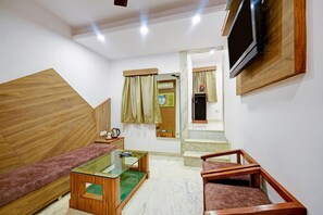 Een moderne woonkamer met een bank, een glazen salontafel, een aan de muur bevestigde televisie en een houten trap die naar een andere kamer leidt.