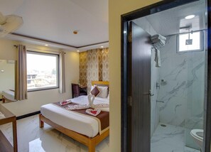 Ein Hotelzimmer mit Bett, Schreibtisch, Stuhl, Duschbereich und Blick auf die Stadt.